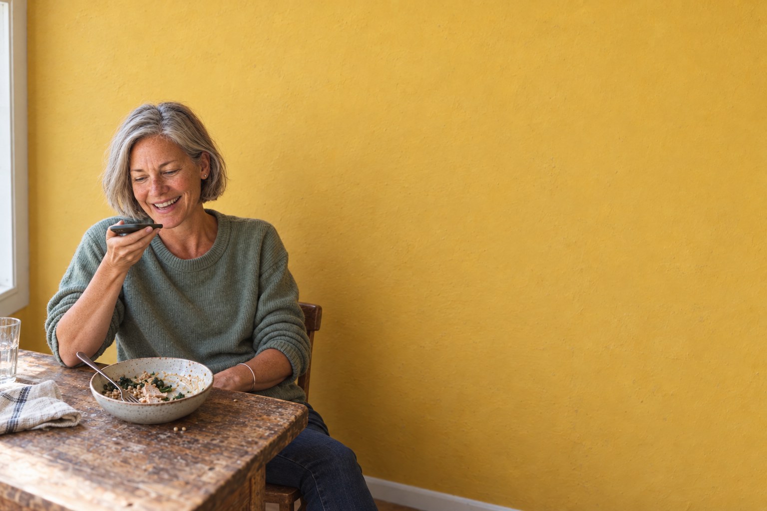 A woman laughing as she tells her phone what's in her grain bowl